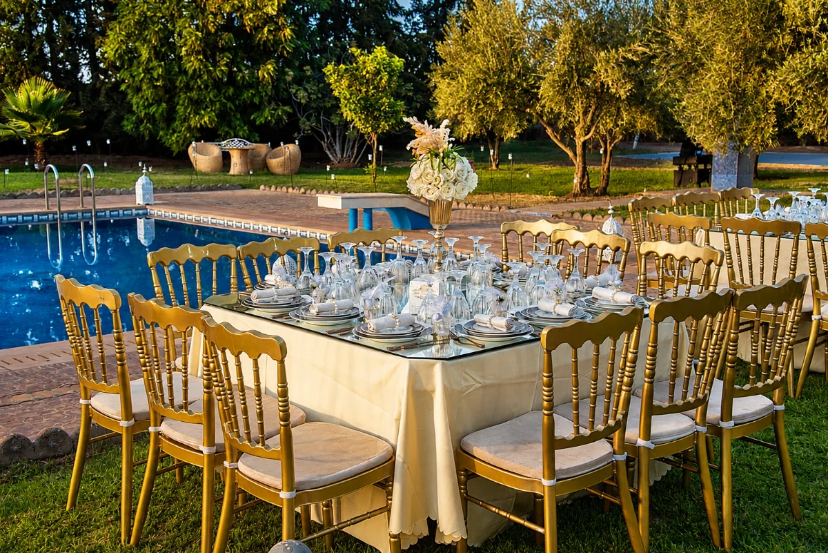 Tables de cocktail et chaises dorées au bord de la piscine — réception de mariage à la Villa Dar Moudar près de Marrakech