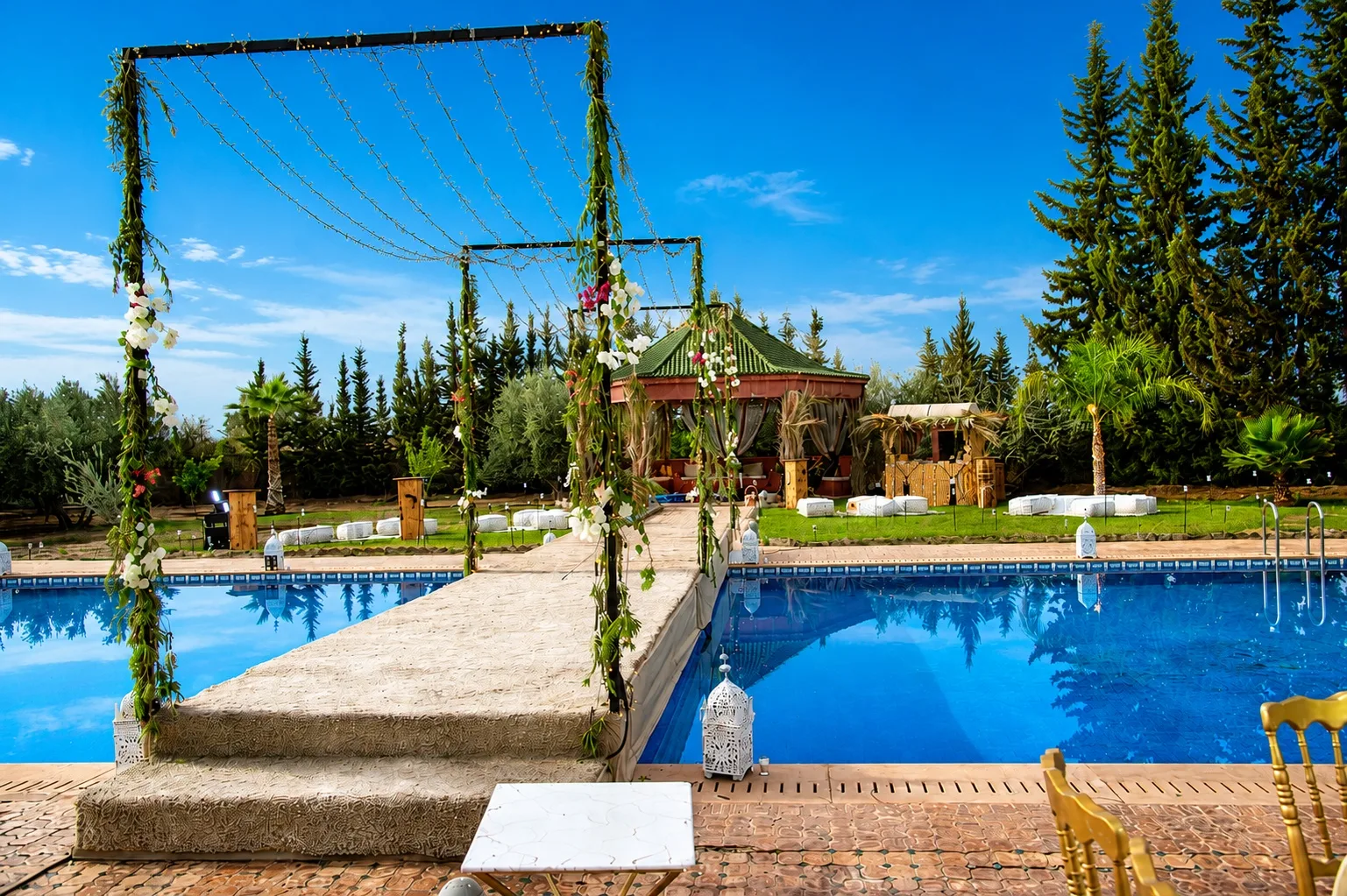 Cérémonie de mariage à la Villa Dar Moudar — passerelle fleurie au-dessus de la piscine et tente caïdale, mariage de luxe à Marrakech