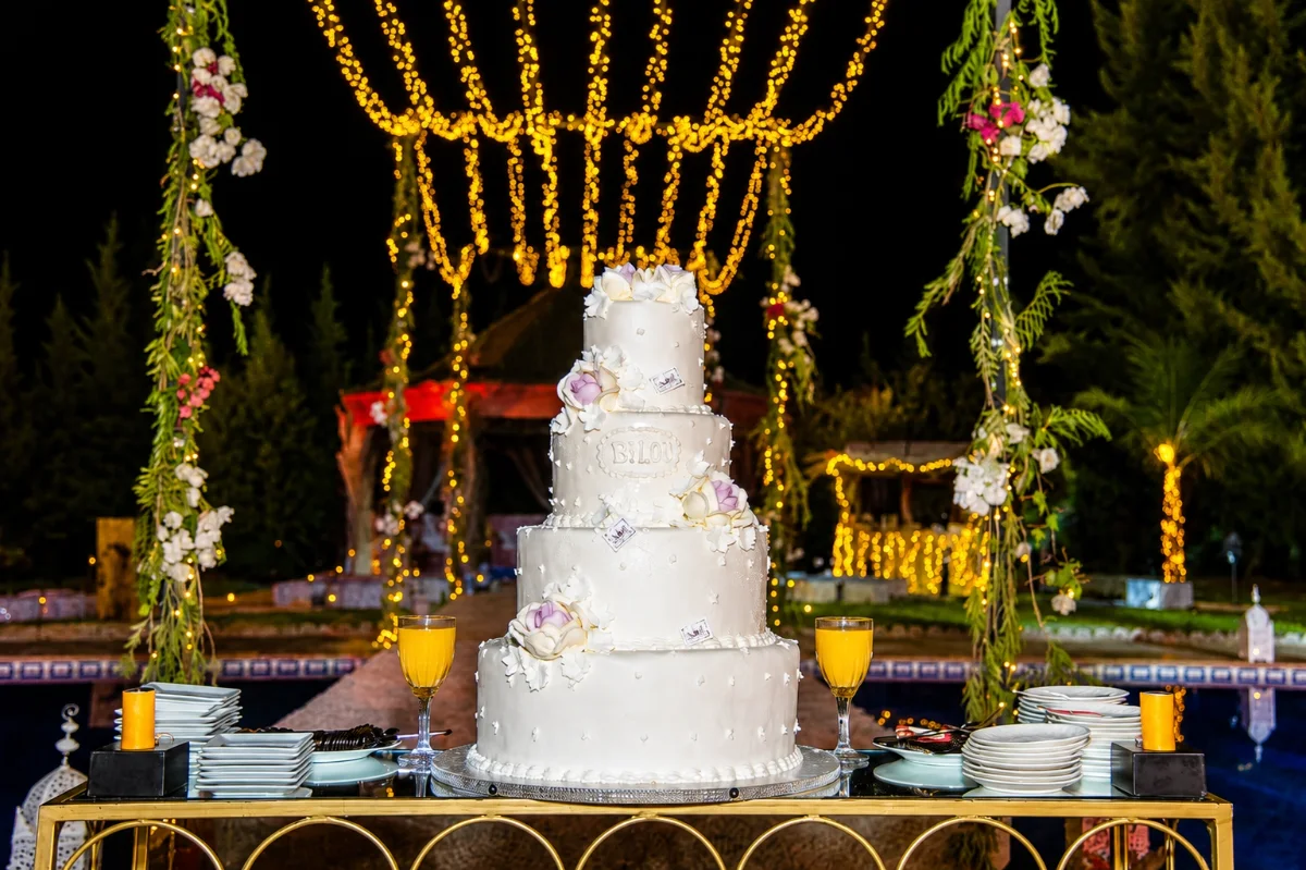 Gâteau de mariage illuminé en soirée sous les guirlandes lumineuses — mariage féérique à la Villa Dar Moudar Marrakech
